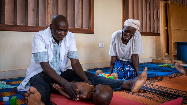 Ein Arzt und eine Ärztin aus dem Rehabilitationszentrum in Bangui in der Zentralafrikanischen Republik behandeln ein Kind, das unter den Folgen frühkindlicher Mangelernährung leidet, mithilfe von phsiotherapeutischen Maßnahmen.