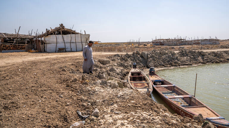 Ein Mann im Irak läuft über die ausgetrocknete Erde zu seinem Ruderboot in einem kleinen See.