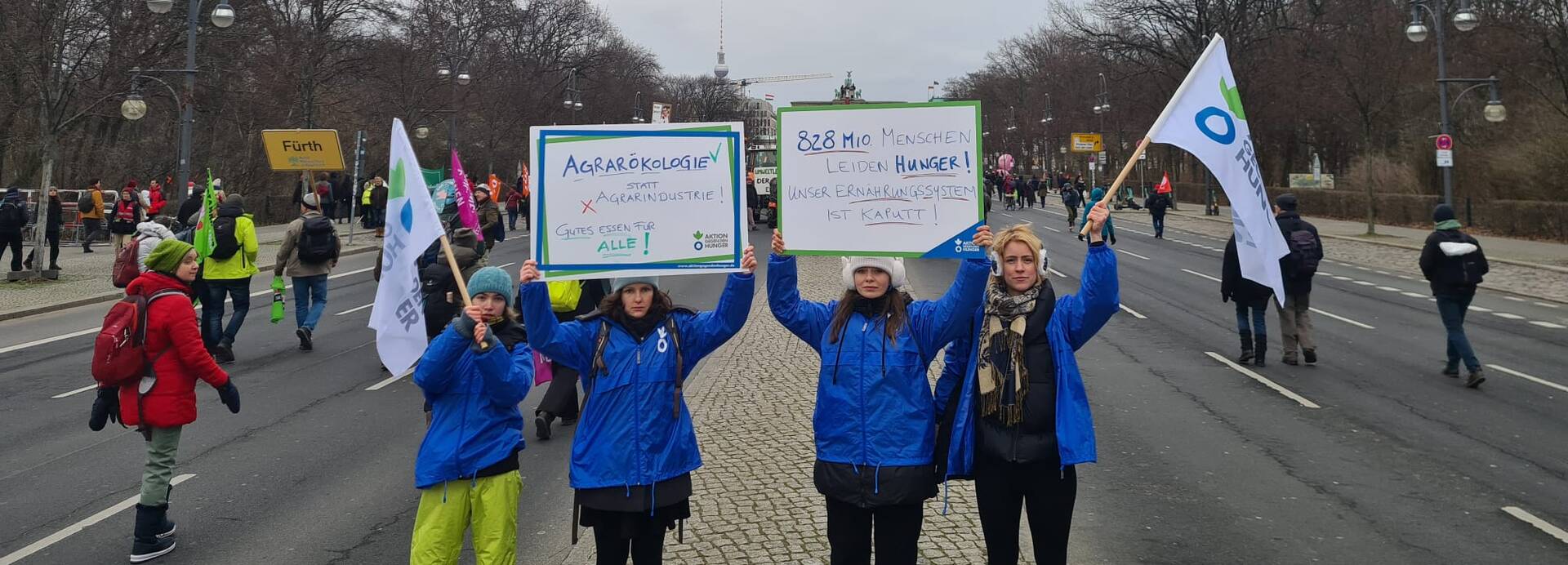 Vier Mitarbeiterinnen von Aktion gegen den Hunger halten im Januar 2023 Demoschilder und Flaggen auf der "Wir haben es satt!"-Demo hoch.