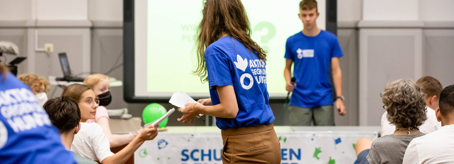 Ein Bildungsvortrag von Schulen gegen den Hunger: Mitarbeiter*innen verteilen Materialien und zeigen eine interaktive Präsentation.