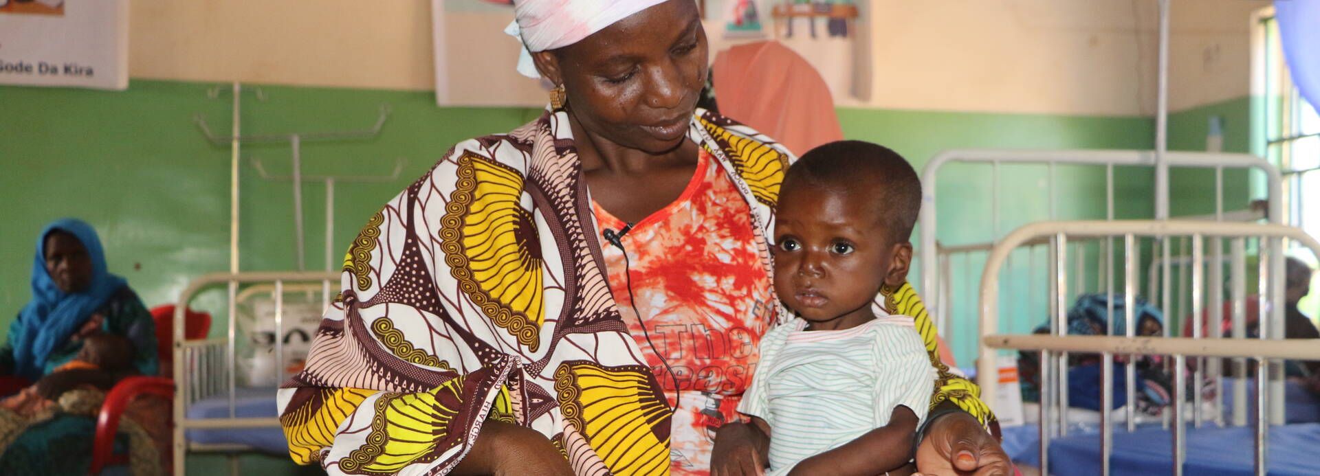 Eine Mutter sitzt mit ihrem Kind auf einem Stuhl in einem stationären Ernährungszentrum in Niger.