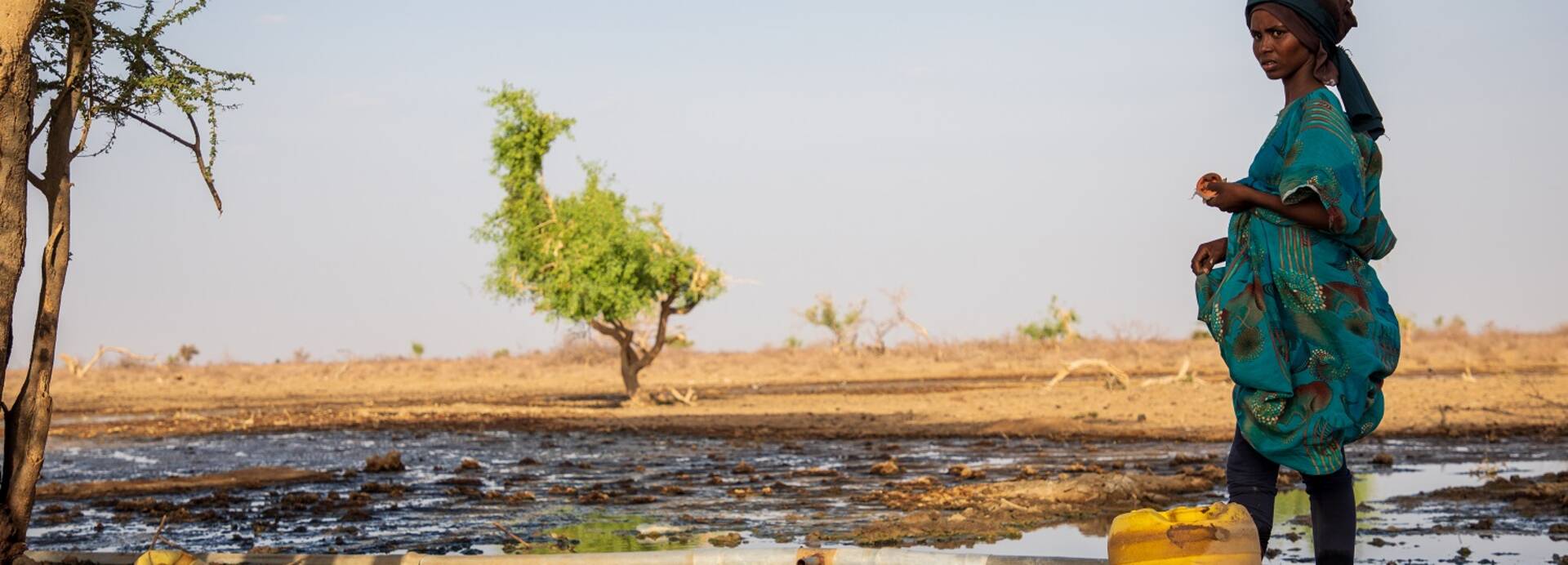 Eine Frau steht in einer trockenen Landschaft in Kenia am Rande eines Wasserlochs.