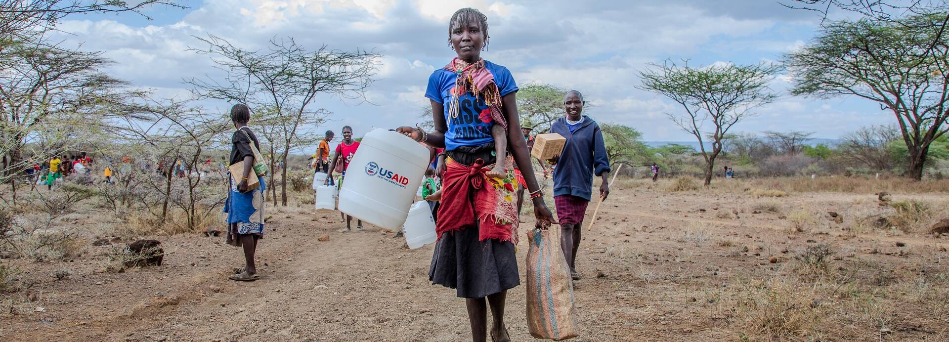 Eine Frau trägt einen Wasserkanister mit der Aufschrift "USAID".