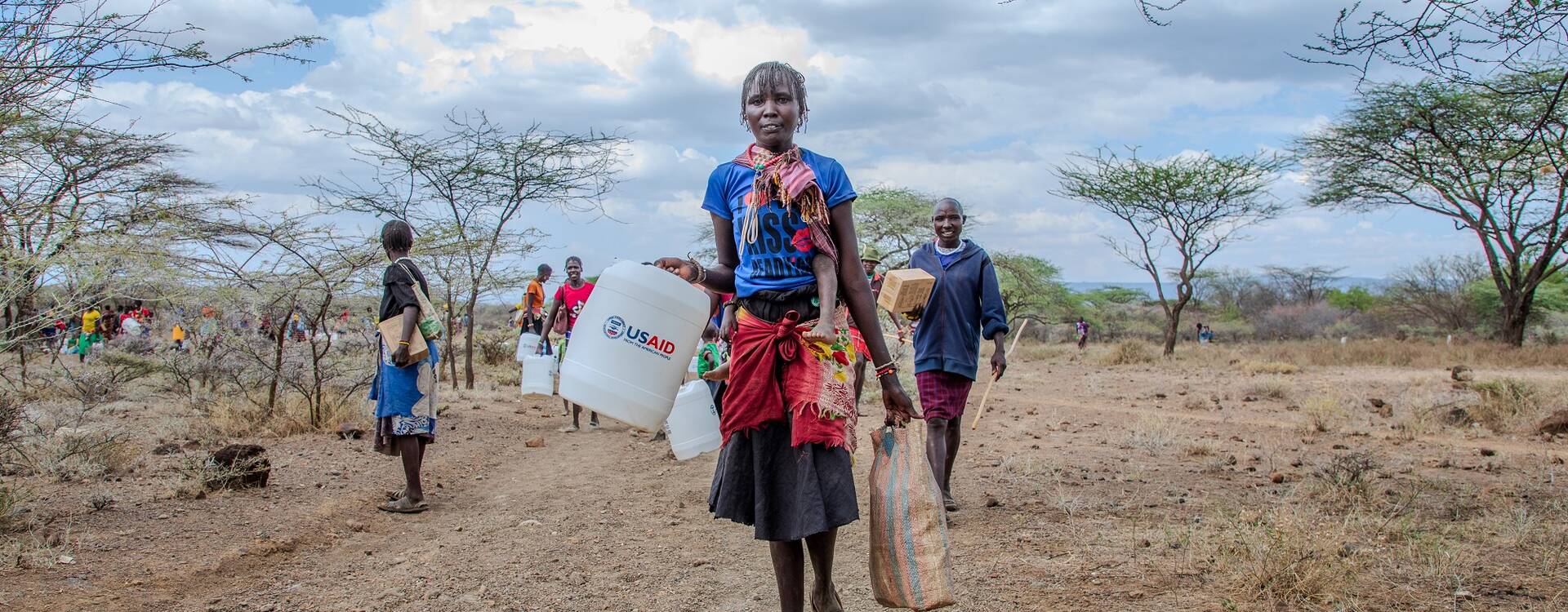 Eine Frau trägt einen Wasserkanister mit der Aufschrift "USAID"