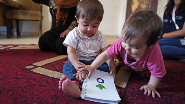 Danas Zwillinge Nagham und Akram spielen mit einem Notizbuch von Aktion gegen den Hunger auf einem Teppich in ihrer Unterkunft im Südlibanon.