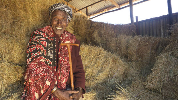 Elimule sitzt lachend im Lagerhaus zwischen Heuballen, die sein Vieh ernähren und seiner Familie ein neues Leben ermöglichen. 