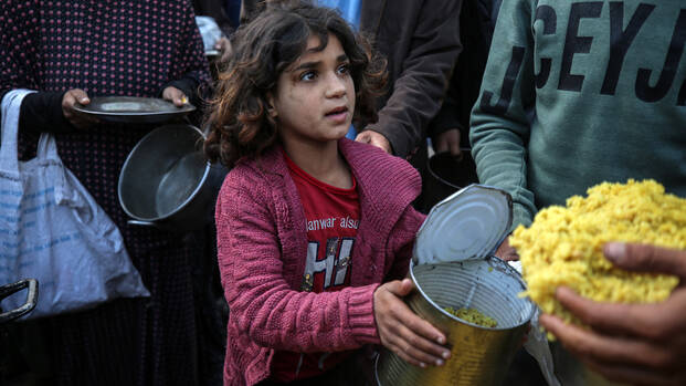 Ein Mädchen im Gazastreifen hält eine geöffnete Dose mit Nahrung in der Hand.