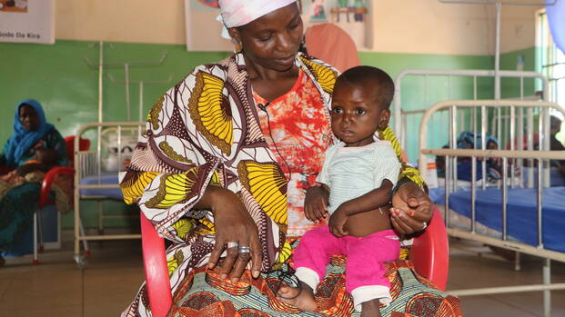 Eine Mutter sitzt mit ihrem Kind auf einem Stuhl in einem stationären Ernährungszentrum in Niger.