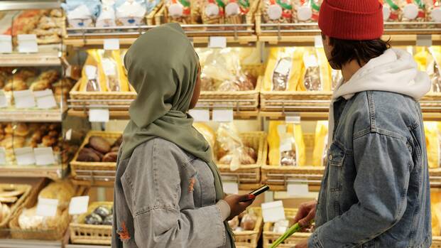 Zwei Menschen stehen vor einem Brotregal in einem Supermarkt.