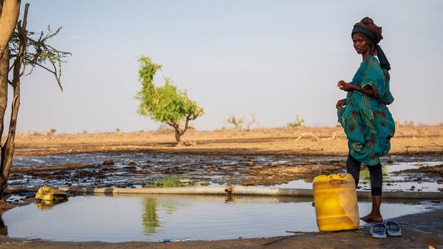 Eine Frau steht in einer trockenen Landschaft in Kenia am Rande eines Wasserlochs.