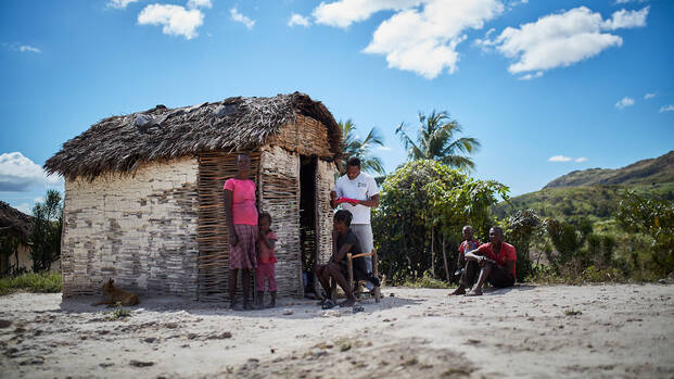 Ein Mitarbeiter von Aktion gegen den Hunger spricht vor einer kleinen Hütte mit einer Familie aus Haiti.