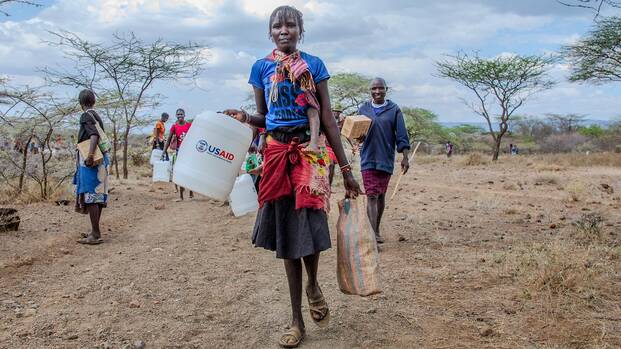 Eine Frau trägt einen Wasserkanister mit der Aufschrift "USAID".